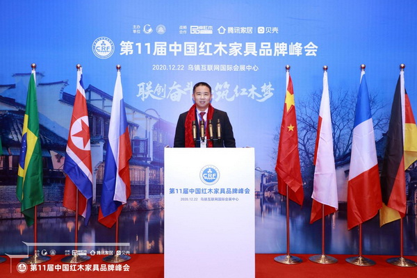 老周家居董事长周仲坚在第11届中国红木家具品牌峰会主题展板前留影 老周家居董事长周仲坚在第11届中国红木家具品牌峰会主题展板前留影